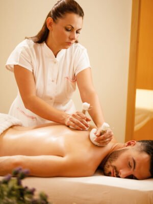Female therapist using herbal balls while massaging man's back at the spa.